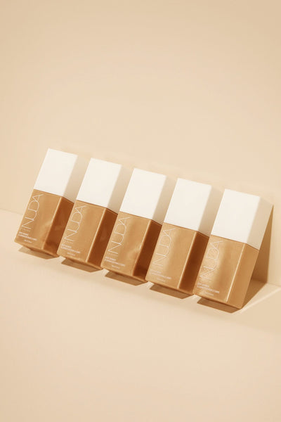 Five bottles of self tanning mousse on a beige background for customizable glowing skin.