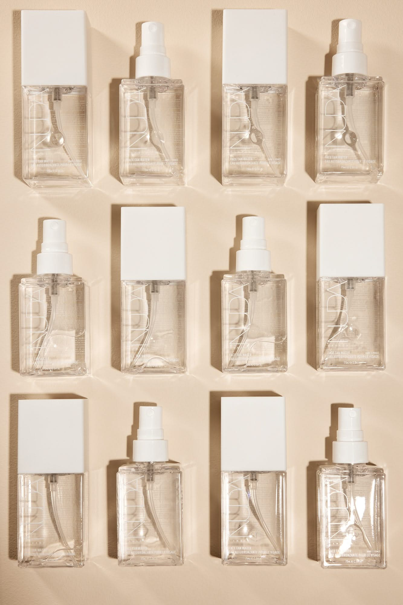 twelve clear spray bottles with white caps arranged in a grid pattern on a light background.