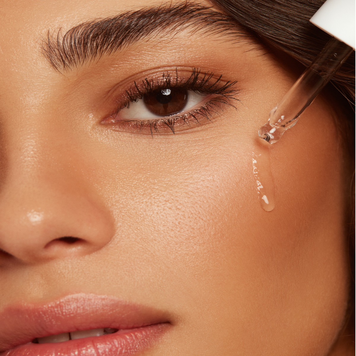 Close-up of a woman applying Hyaluronic Self Tanning Serum to her cheek, showcasing radiant, glowing skin.