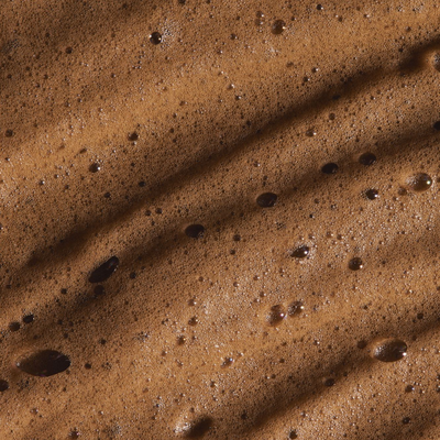 Close-up of rich brown self-tanning mousse showing smooth texture and bubbles, ideal for achieving a radiant tan.