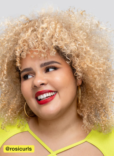 Smiling person with curly blonde hair wearing hoop earrings and a bright yellow top.