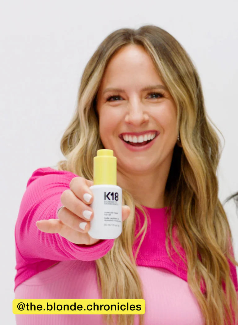 Smiling woman in pink holding K18 hair product, showcasing its benefits for hair repair and conditioning.