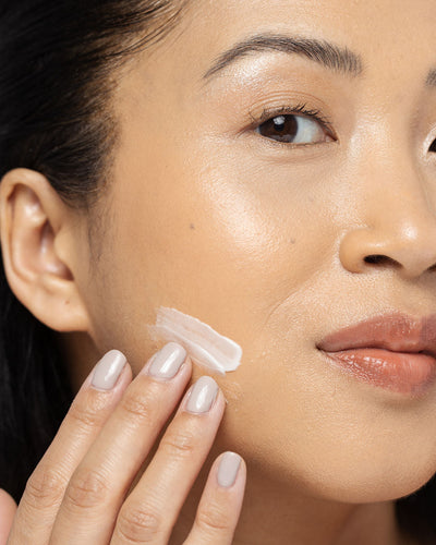 Woman applying AHA/BHA exfoliating cream to her face, showcasing a smooth and radiant complexion.