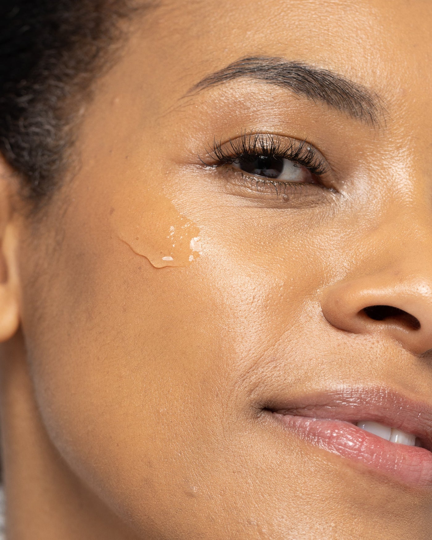 Close-up of a woman with glowing skin applying a gentle gel cleanser for all skin types.