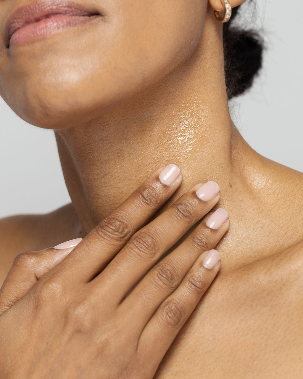 Close-up of a woman applying Kine-C serum on her neck for hydration and anti-aging benefits.