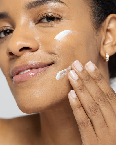 Woman applying skincare product to her cheek, showcasing radiant skin and healthy complexion.