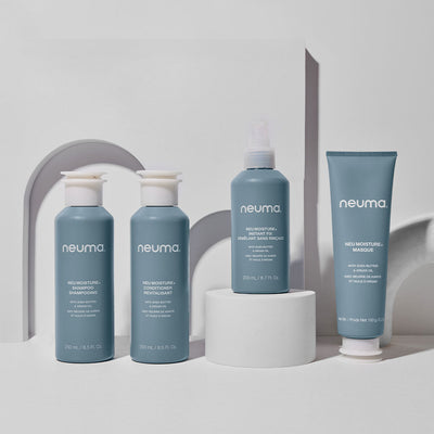 Neuma Moisture hair care products including shampoo, conditioner, and mask displayed on a modern pedestal.