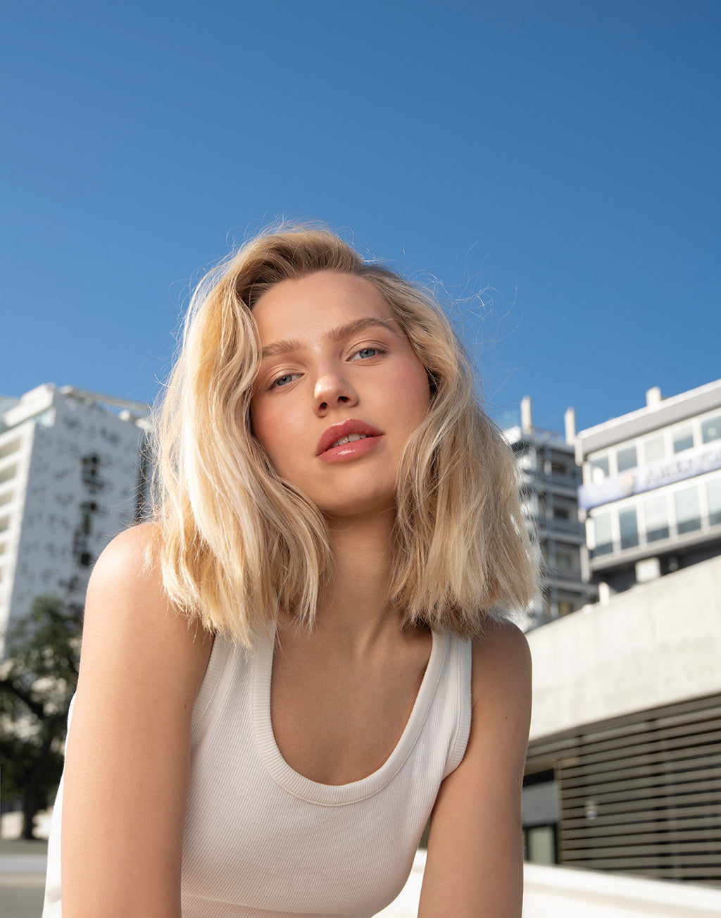 Young woman with blonde hair smiling outdoors, showcasing vibrant and healthy hair in a clear blue sky.