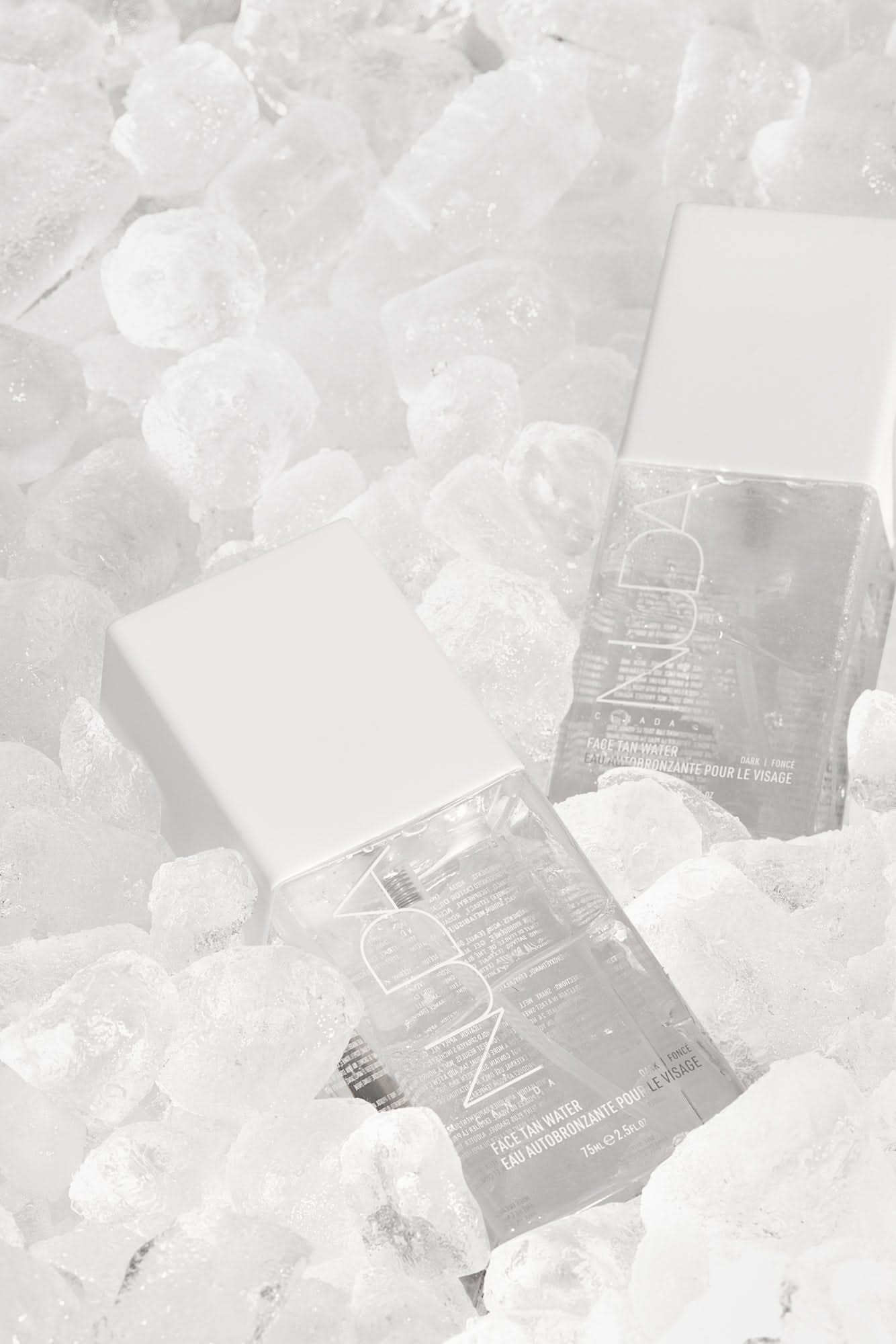 Two skincare bottles nestled in ice, showcasing a refreshing and cooling aesthetic for beauty enthusiasts.