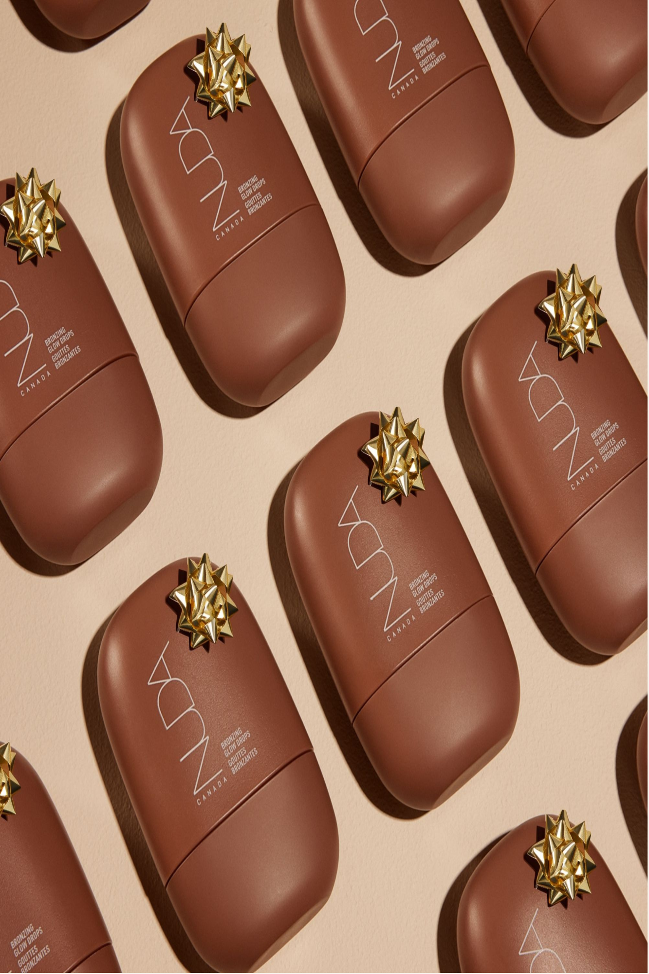 NUDA Bronzing Glow Drops in festive packaging, featuring golden star bows on elegant brown bottles.