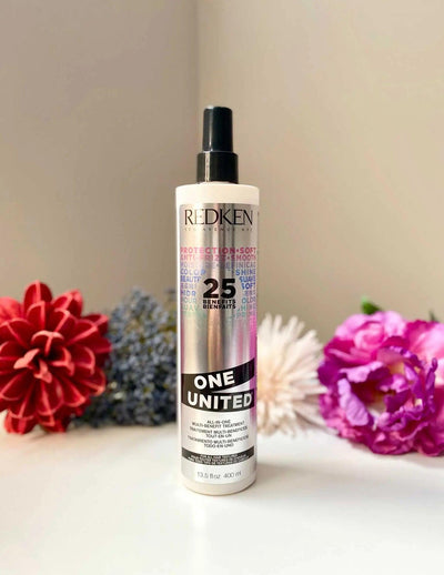 Redken One United multi-benefit hair treatment spray surrounded by colorful flowers, ideal for all hair types.