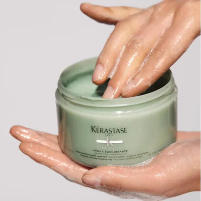 Hands applying Kerastase Argile Équilibrante purifying clay shampoo for oily hair and scalp care.