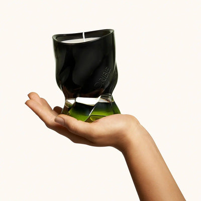 Oribe Desertland scented candle held in a hand, showcasing its unique modern design and vibrant green base.